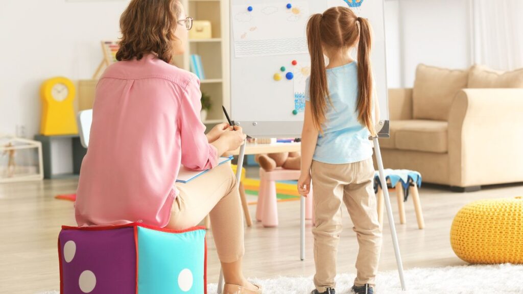 An RBT registered behavioral technician monitors a young girl client as she paints pictures on an easel.